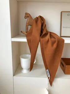Primer plano de un pañuelo triangular de lana pura color caramelo en un estante.