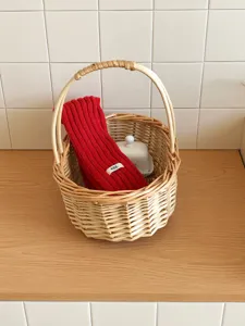 Detalle de bufanda tejida roja en cesta de mimbre mostrando textura acanalada y etiqueta.