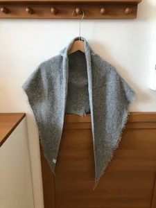 Detail view of the cozy grey wool triangular scarf with soft fringe edges for winter warmth.
