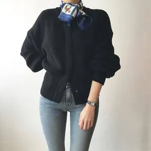 Detail shot of an elegant silk scarf with a horse motif worn with a black cardigan and jeans.