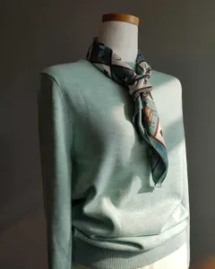 Vista detallada del jersey de punto verde menta con elegante fular de seda con caballos.