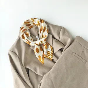 Detailed view of a pleated polka dot square scarf beautifully styled with a neutral suit jacket.