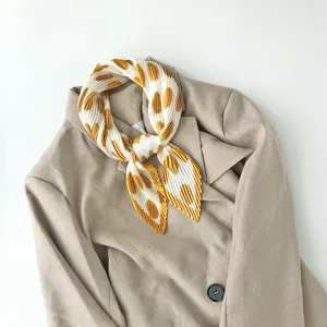 Detailed shot of pleated polka dot small square scarf tied neatly on neutral blazer collar.