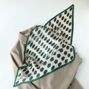 Detailed view of a pleated square scarf with green polka dots on pink, elegant neckerchief style.
