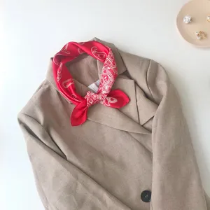 Detailed shot of a stylish red paisley silk square scarf elegantly tied on a beige blazer collar.