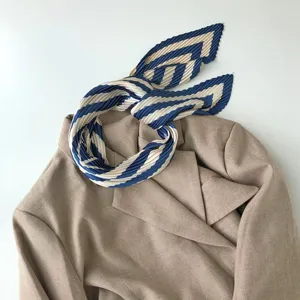 Detailed shot of a pleated geometric striped silk scarf elegantly tied on a camel blazer.