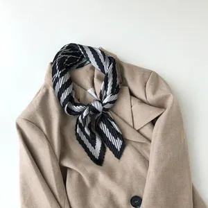 Close-up detail of a black and white pleated geometric scarf styled on a chic beige blazer.