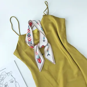 Detailopname van een gele slipdress gecombineerd met een bedrukte smalle zijden sjaal.