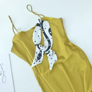 Gedetailleerde close-up van mosterdgele slipdress gecombineerd met een slangenprint sjaal.