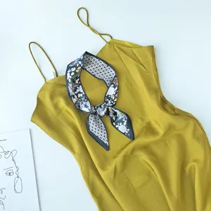 Gedetailleerd uitzicht van gele slipdress gecombineerd met geprinte zijden sjaal op wit vlak.