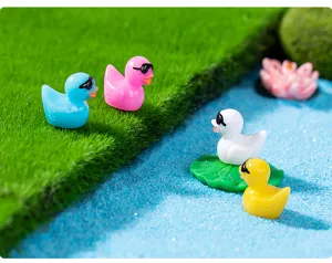 Gros plan de petits canards en resine colores avec lunettes de soleil sur mousse et sable.