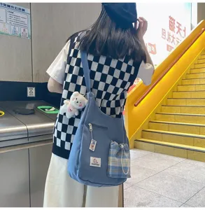 Vue détaillée du sac bandoulière en toile bleue avec poche à cordon et charm ours.