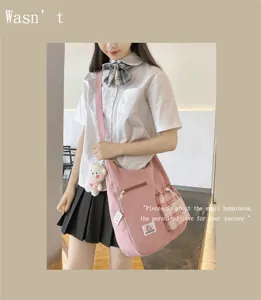 Vue détaillée du sac bandoulière rose en toile avec poche à carreaux et pendentif ours.
