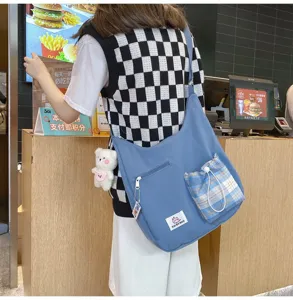 Détail de sac bandoulière en toile, style messager décontracté avec poche à carreaux et ours.