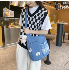 Vue détaillée du sac bandoulière en toile bleue avec poche à carreaux et pendentif.
