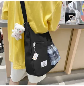 Vue détaillée du sac bandoulière en toile noire avec poche à carreaux et charmant petit ours.