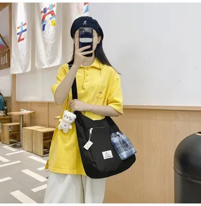 Sac bandouliere en toile noire avec une poche carree et pendentif de peluche ourson.