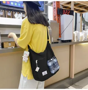 Vue détaillée d'un sac bandoulière en toile noire avec poche à carreaux et pendentif.