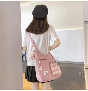 Détail du sac bandoulière rose en toile avec poche à carreaux et pendentif ours en peluche.