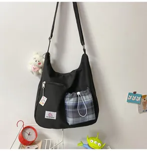 Vue de détail du sac bandoulière noir avec poche avant à carreaux bleus et pendentif.