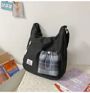Vue de détail du sac bandoulière en toile noire avec poche avant à cordon à carreaux.