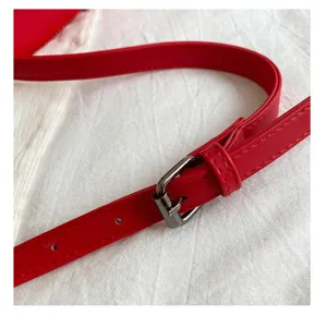 Primo piano dettaglio di tracolla per borsa in pelle PU rossa con fibbia metallica.
