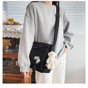 Detail shot of black canvas crossbody bag with plush bear pendant and adjustable strap.
