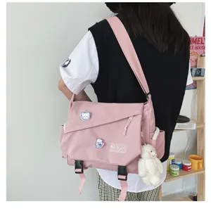 Pink canvas messenger bag detail shot featuring cute bear pendant and badges, student style.