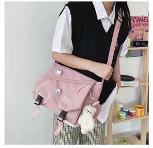 Pink canvas messenger bag detail shot, featuring front buckle and cute plush bear pendant.