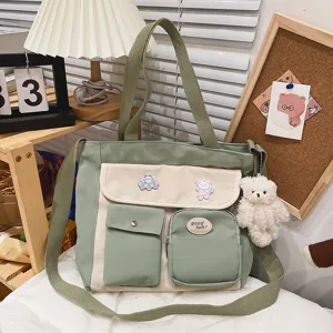 Sage green canvas tote bag detail view showing front pockets, cute plush bear pendant and pins.