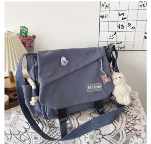 Detail view of the stylish grey canvas messenger bag featuring brand label and cute bear pendants.