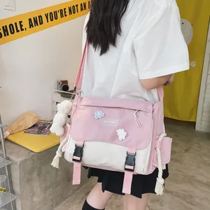Detail view of the pink and white canvas messenger bag with cute badges and plush bear charm.