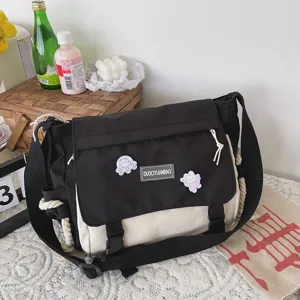 Detailed shot of black and white canvas messenger bag with flap closure and cute cartoon pins.