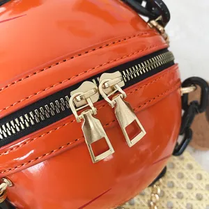 Close-up detail of glossy orange sphere purse, golden dual zippers and black acrylic chain.