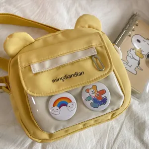Nahaufnahme der gelben Bärenumhängetasche mit transparenter Tasche und Ansteckern.
