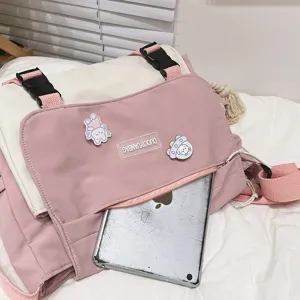 Detail view of a cute pink and white canvas messenger bag with cartoon pins and front pocket.