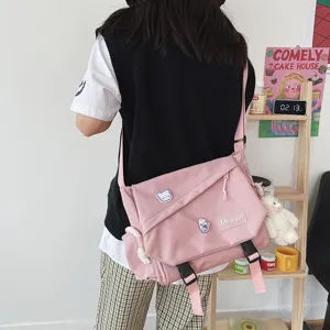 Pink canvas messenger bag detail showing cute badges, plush pendant and durable buckle closure.