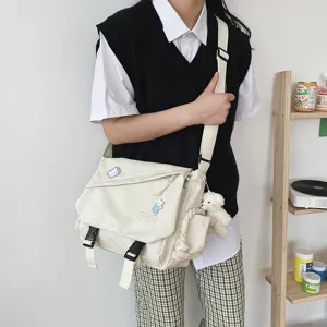Detailed view of cream canvas crossbody messenger bag with cute bear pendant and strap.
