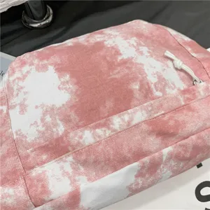 Primo piano di una borsa a tracolla in tela tie-dye rosa con dettagli di trama e zip bianca.