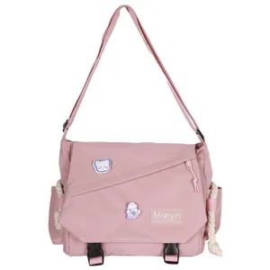 Pink canvas messenger bag detail showing cute cartoon patches, adjustable strap and front buckle.