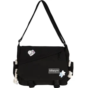 Black canvas messenger bag detail showing cute bear pins, woven label and buckle closure.