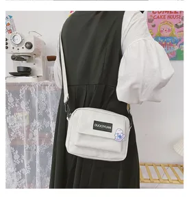 Vista detallada de un bolso cruzado de lona blanca con bolsillo frontal para uso diario y casual.