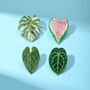 Close up of tropical plant enamel brooch pins featuring monstera and caladium leaf designs.