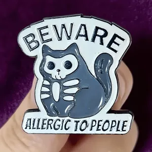 Detail shot of gothic skeleton cat enamel pin, featuring quirky text and smooth finish.