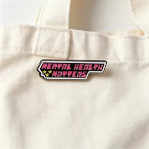 Gros plan détaillé du badge en métal émaillé avec slogan rose vif et accents d'étoiles dorées.