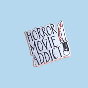 Close-up detail of horror movie addict enamel pin with bloody dagger design and metal texture.
