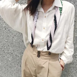 Detail view of the stylish pleated patterned skinny scarf worn on a white shirt, soft texture.