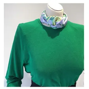 Detail shot of green knit top with elegant purple patterned scarf accessory, soft fabric style.