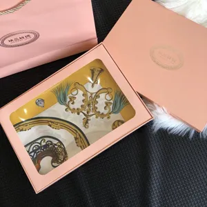 Detailed view of luxury silk square scarf inside pink gift box featuring classic ornate gold patterns.