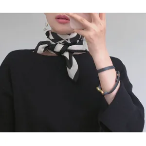 Close-up detail of a chic black and white patterned silk scarf worn around the neck.